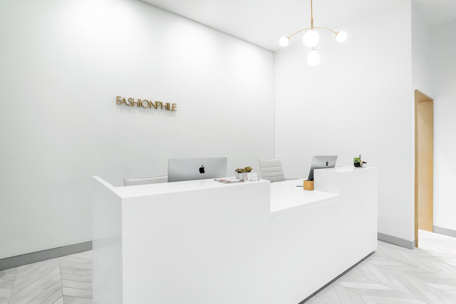 The modern, white reception area of a FASHIONPHILE Selling Studio, with the gold brand logo on the wall.