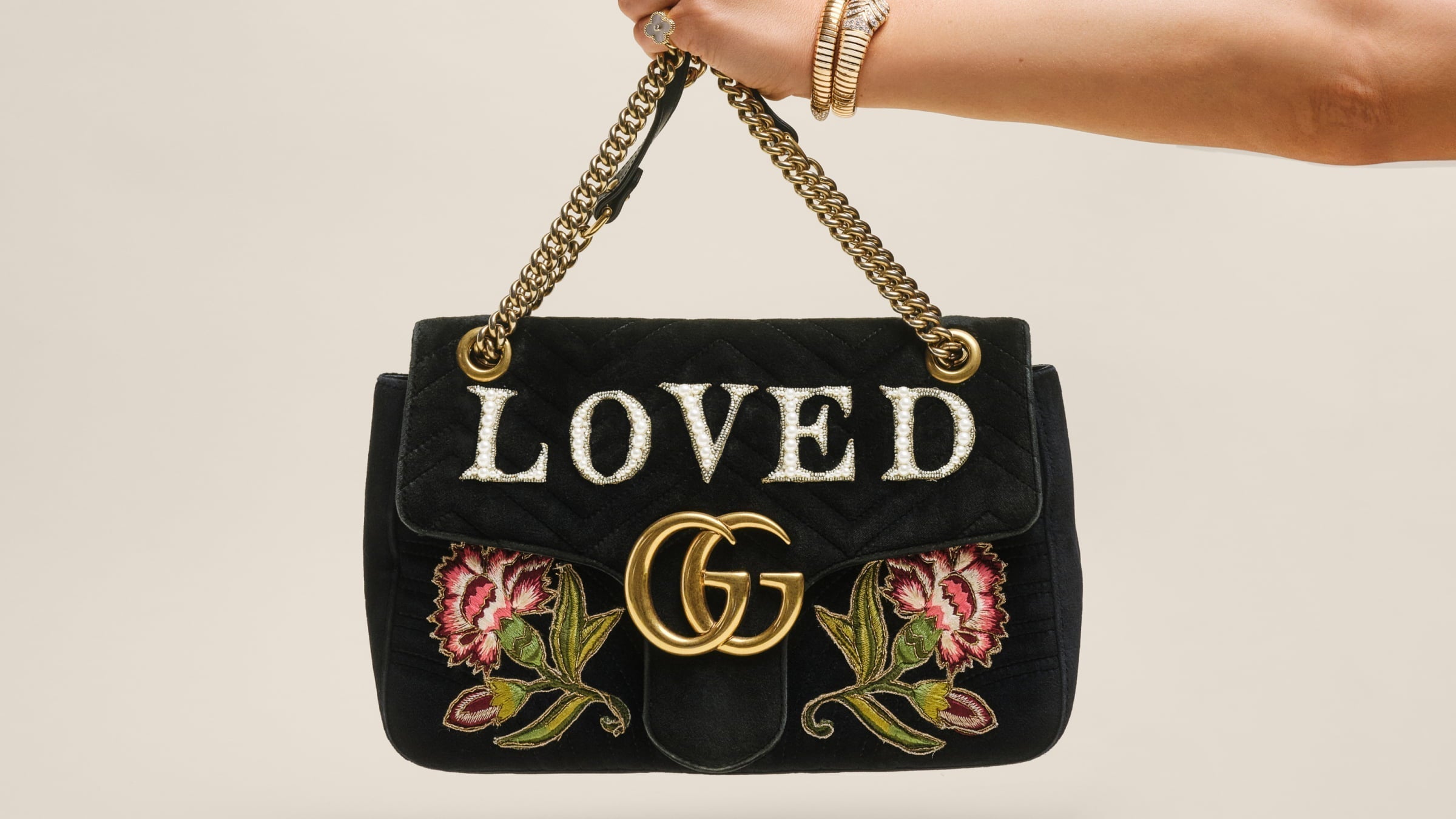 A hand wearing gold jewelry holds up a black velvet Gucci GG Marmont