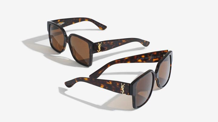 An image featuring two pairs of identical tortoise shell sunglasses with dark brown lenses, arranged on a plain white surface. One pair is positioned slightly behind and above the other, showcasing the gold logo on the side of the thick frames.