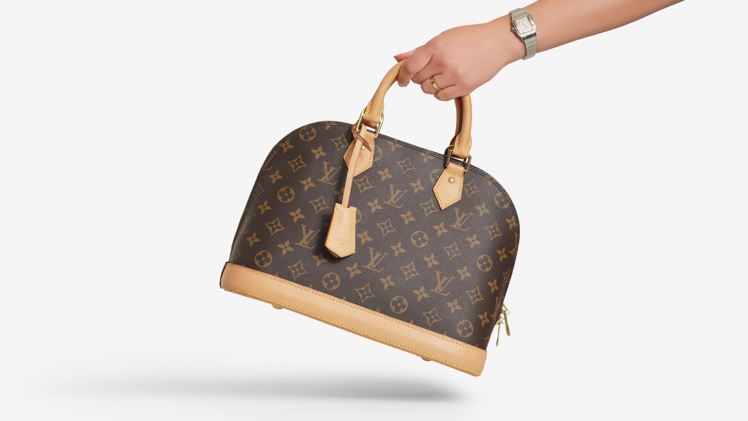 A hand holds a Louis Vuitton Alma bag