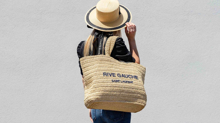 Fashion girl styles her Dior raffia hat with a Saint Laurent woven raffia tote and poses facing back.