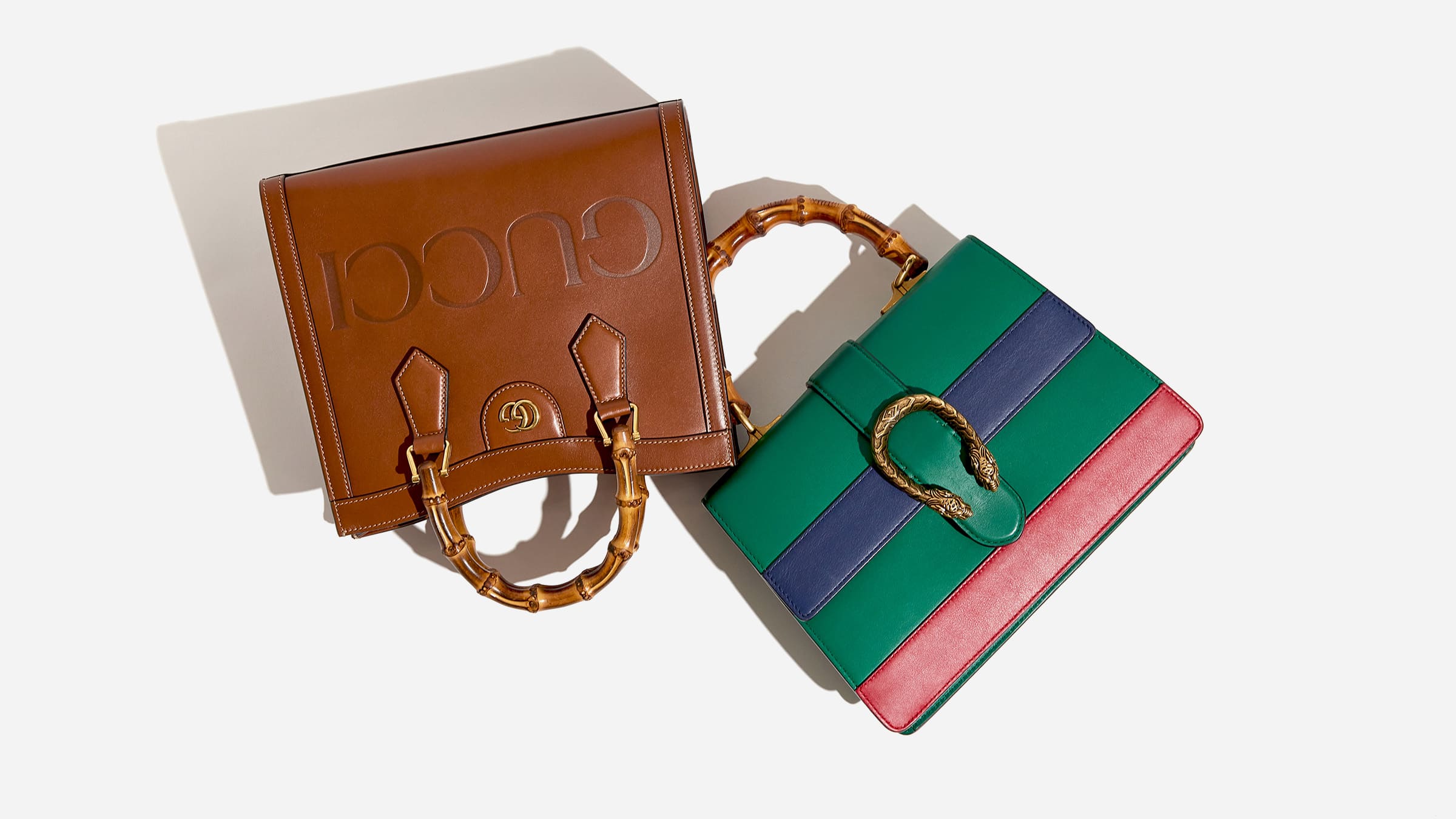 a flat lay image of a brown gucci diana bamboo tote and a tri-color gucci dionysus bamboo bag in the colors green, blue and red by FASHIONPHILE