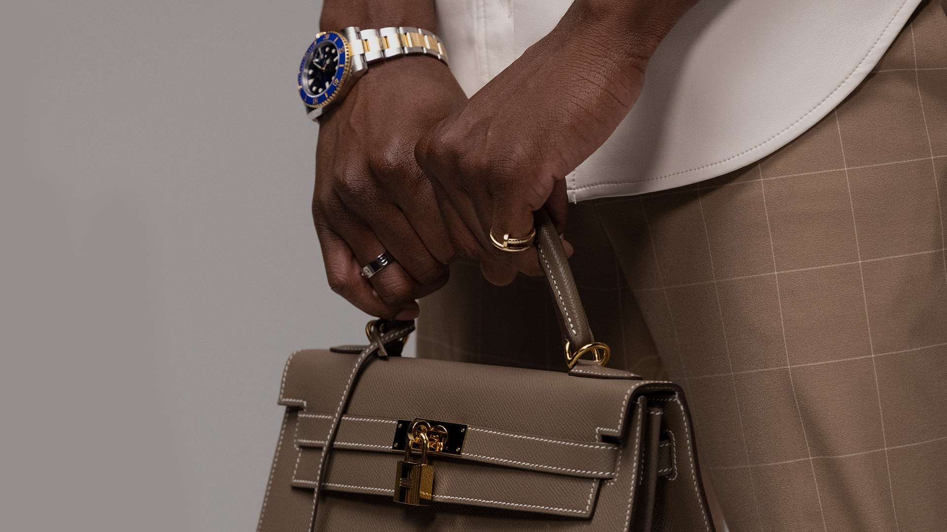 lifestyle image of male model wearing fine jewelry and designer watch holding a Hermes kelly bag FASHIONPHILE