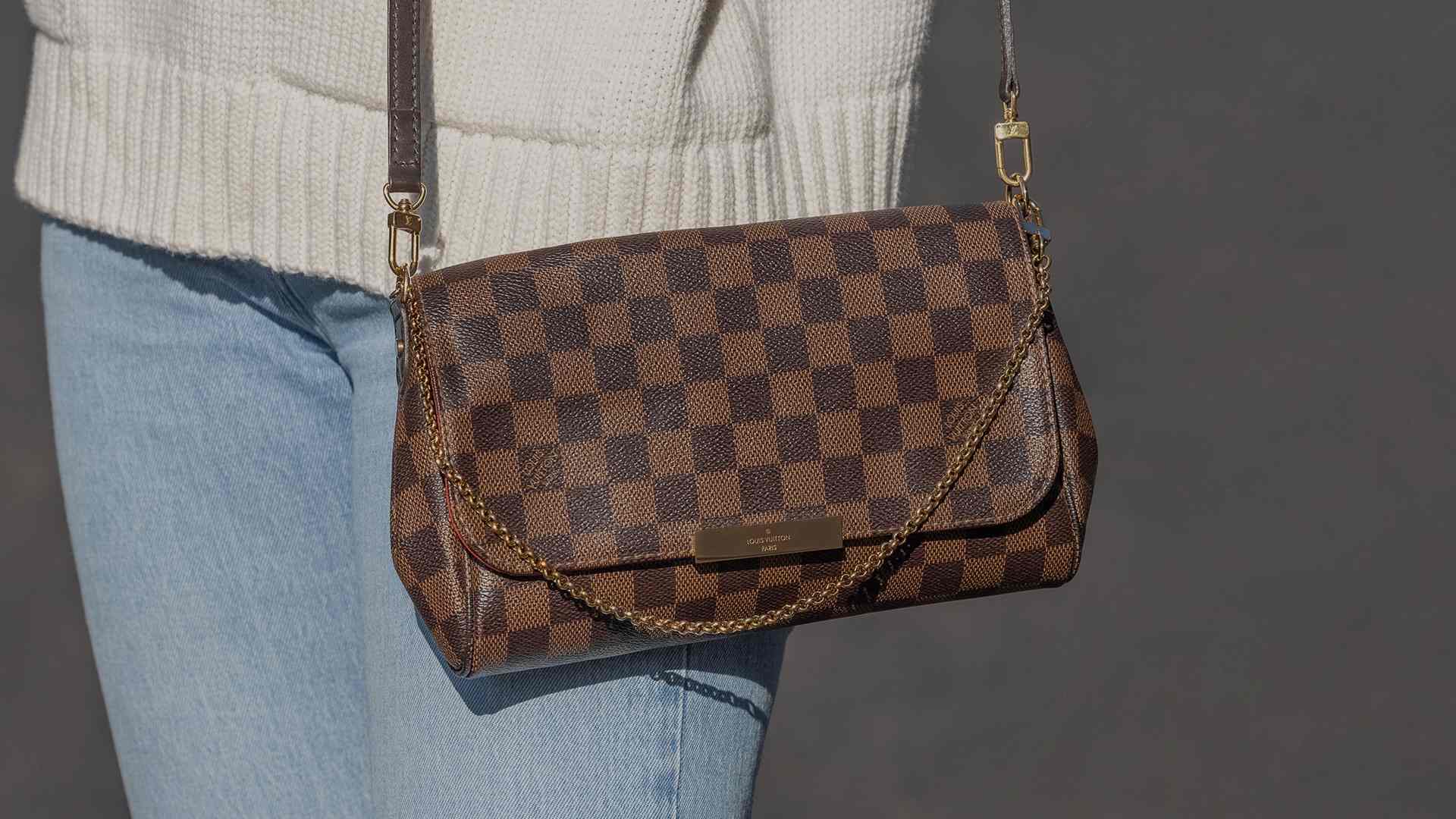 lifestyle image of girl in oversized sweater and jeans wearing her louis vuitton damier ebene favorite mm bag as a crossbody FASHIONPHILE