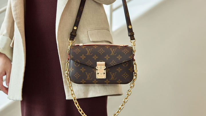 the louis vuitton pochette metis east west bag worn on the arm with the chain strap hanging by FASHIONPHILE