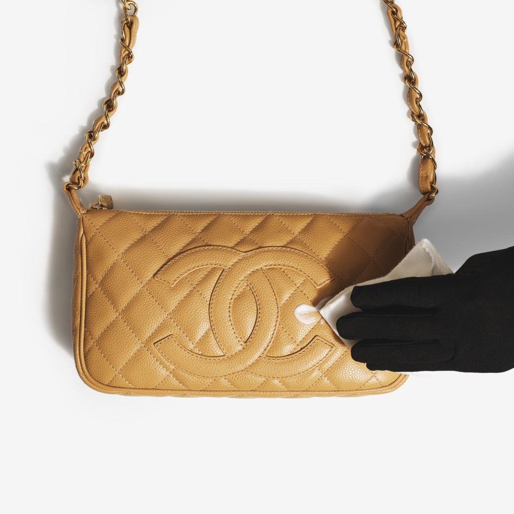 Gloved hands use a premium microfiber cloth to gently buff handbag conditioner on a a Chanel Timeless CC Shoulder Bag. Both the cloth and the conditioner are part of the ReNew Handbag Cleaning Kit.