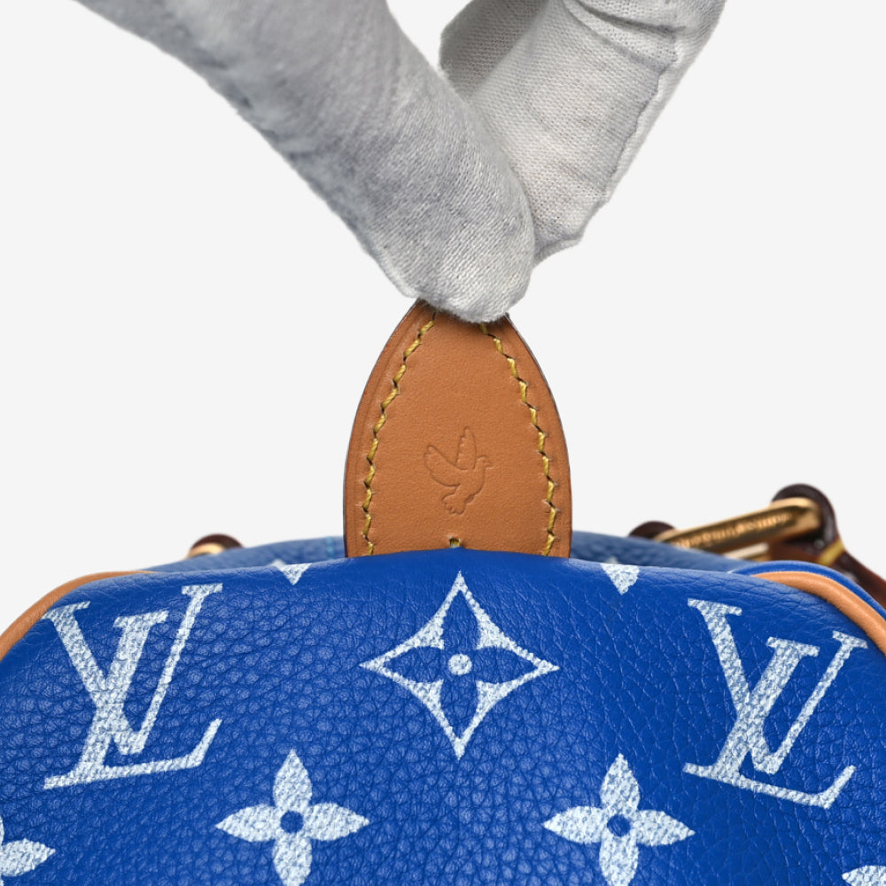 A white-gloved hand lifting the leather tab on a Blue Speedy P9 to reveal the Dove blind stamp