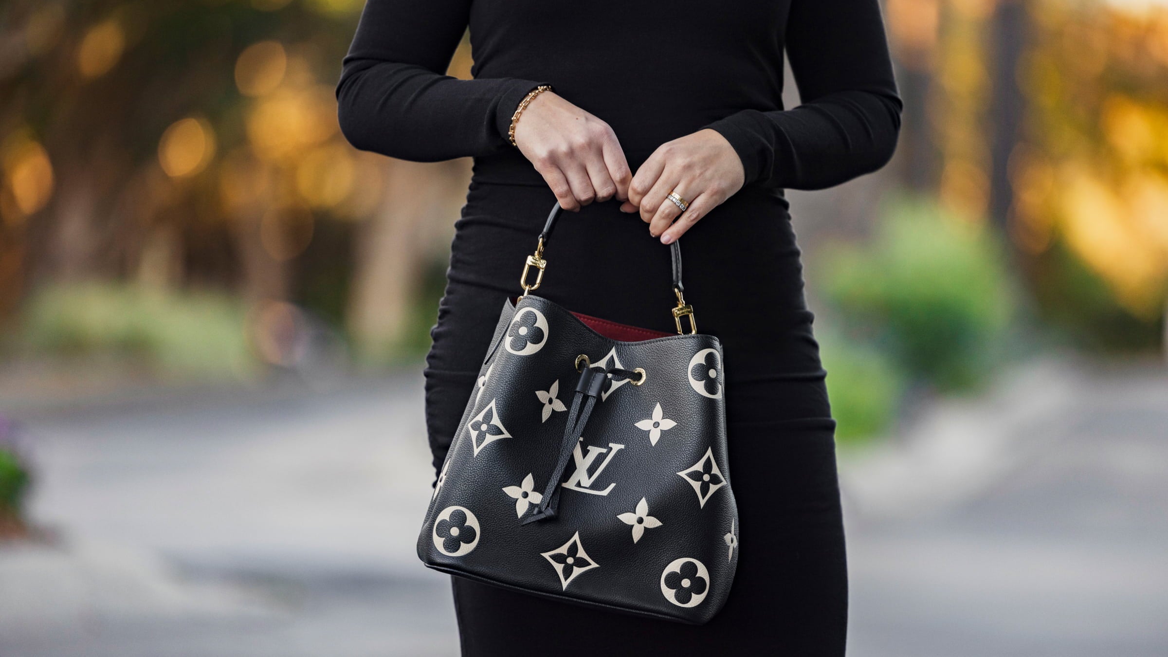 an image taken outside of model wearing a black dress with the LOUIS VUITTON Empreinte Monogram Giant Neonoe MM in the colors Black and Beige by FASHIONPHILE