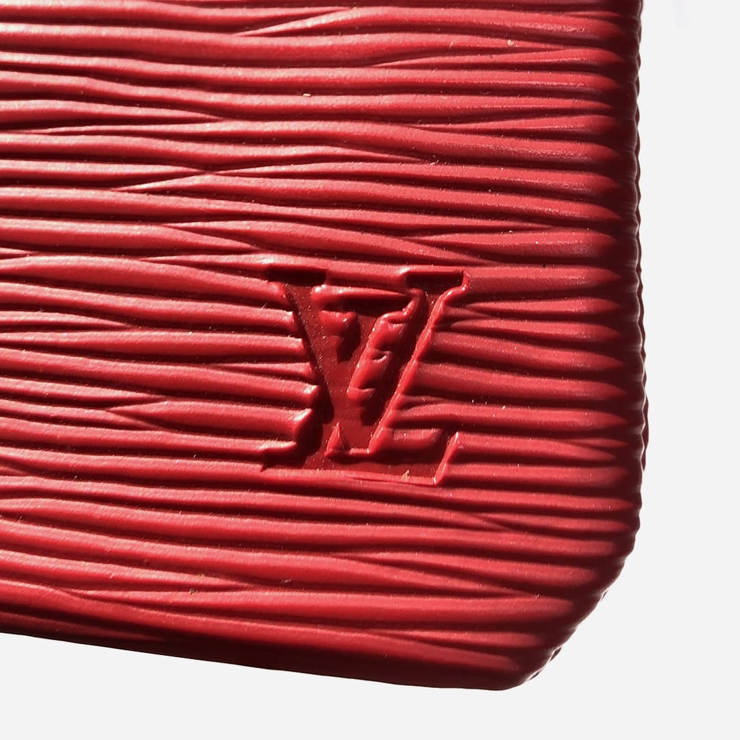 close up image of a fake Louis Vuitton logo debossing at the lower right-hand corner of a Louis Vuitton Epi Leather Key Pouch by FASHIONPHILE