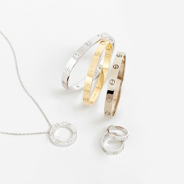 pieces from the cartier love collection including the cartier love bracelets in white gold and yellow gold next to cartier love rings and a necklace by FASHIONPHILE