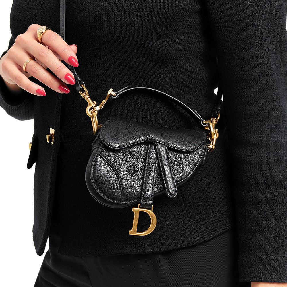 this is an image by fashionphile of a model wearing a black christian dior micro saddle bag as a crossbody