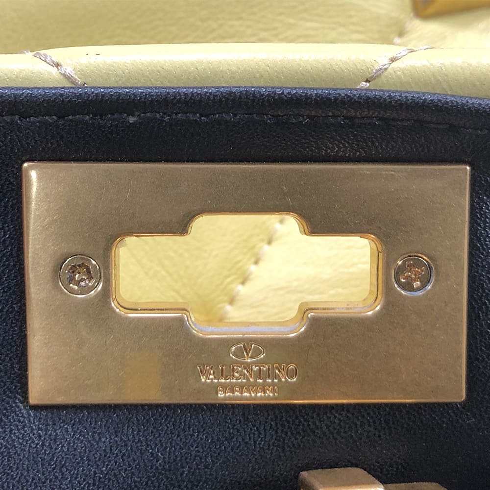 close up image of a fake valentino garavani logo engraving plate on the inside using phillips screws by FASHIONPHILE