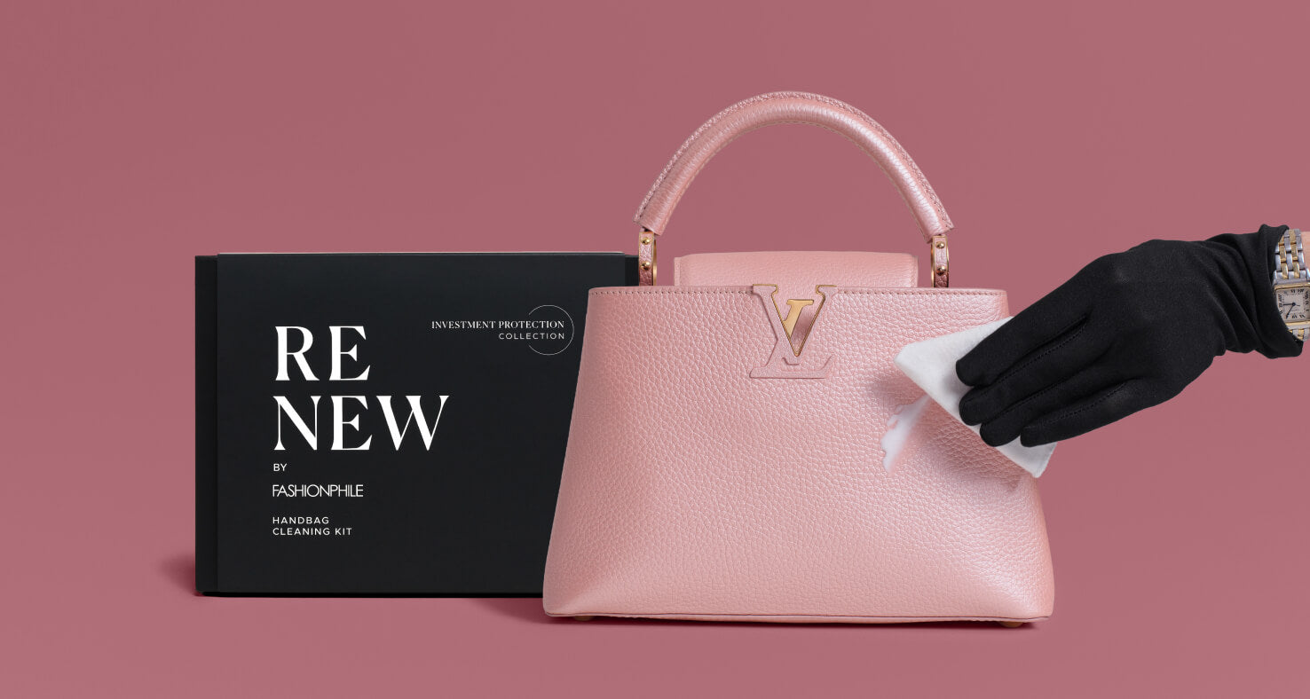 A pink pebbled leather handbag with a gold-tone LV monogram is shown beside a black product box labeled 'RENEW BY FASHIONPHILE'. A black-gloved hand wipes the bag with a white cloth against a dusty pink background.