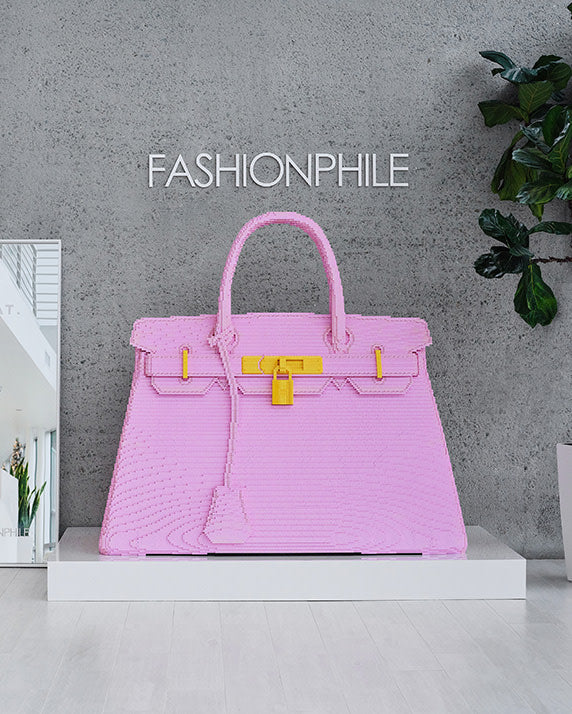 The Flagship San Diego (Carlsbad) entry room with FASHIONPHILE logo in white on a grey wall and sitting below a giant pink Lego Birkin bag