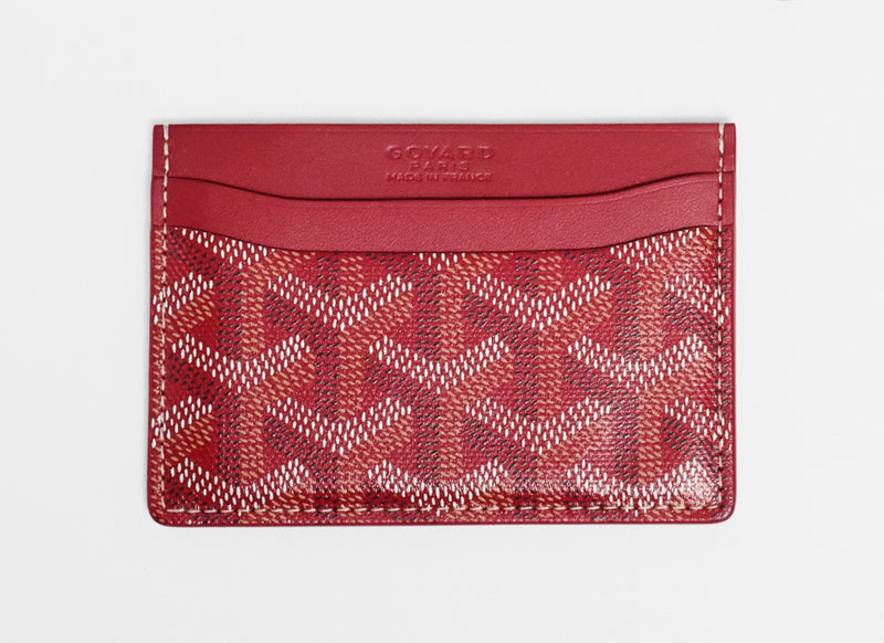 A red Goyard card holder wallet featuring the brand's signature monogram pattern on the lower half and a smooth red leather top band with debossed branding, shown on a plain white background.