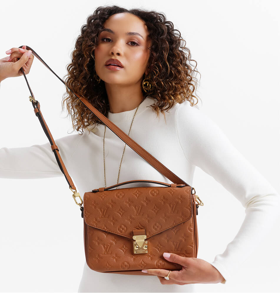 A woman wearing a white mock-neck top holds a brown embossed leather shoulder bag with a gold clasp and strap against a clean white background.
