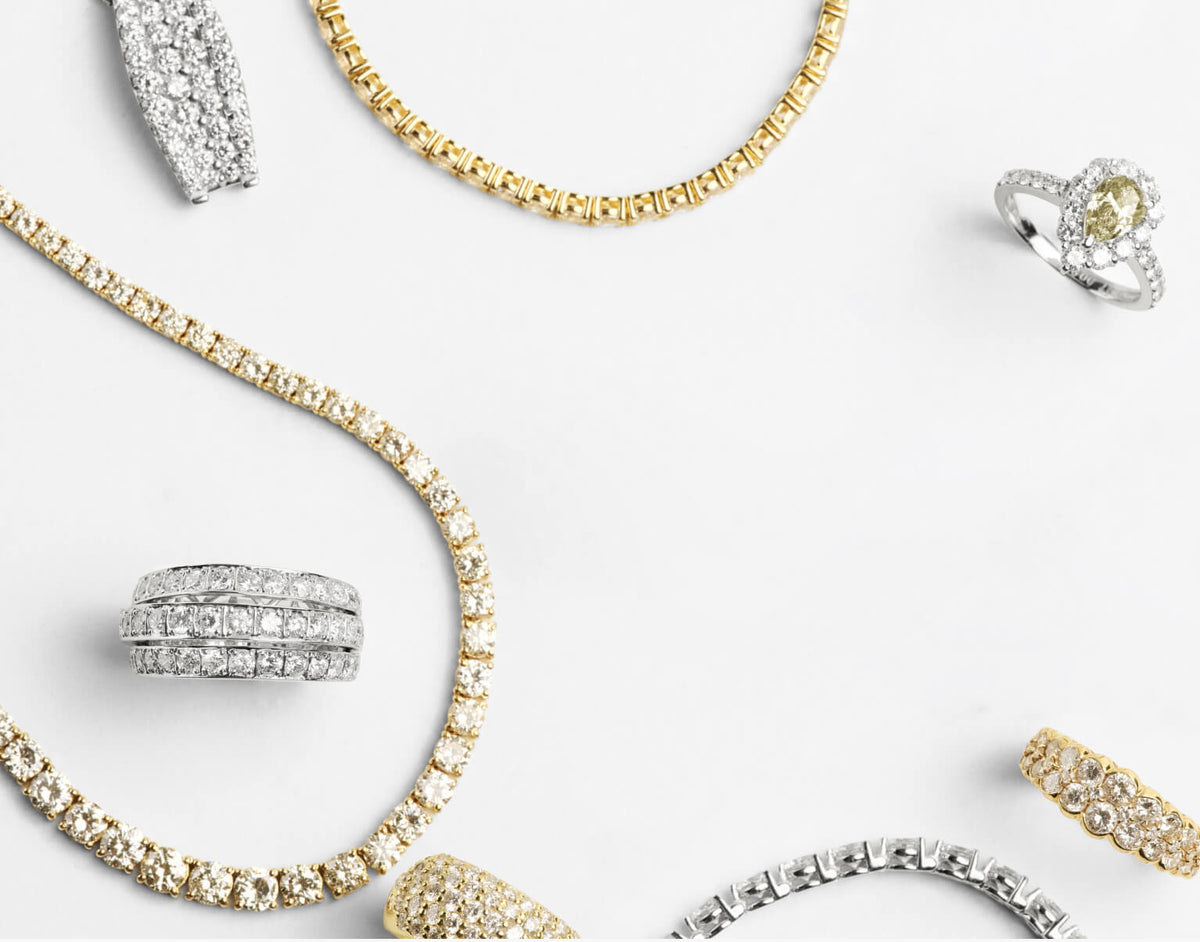 An assortment of yellow gold and silver diamond jewelry, including necklaces, rings, and a bracelet, arranged elegantly on a clean white background.