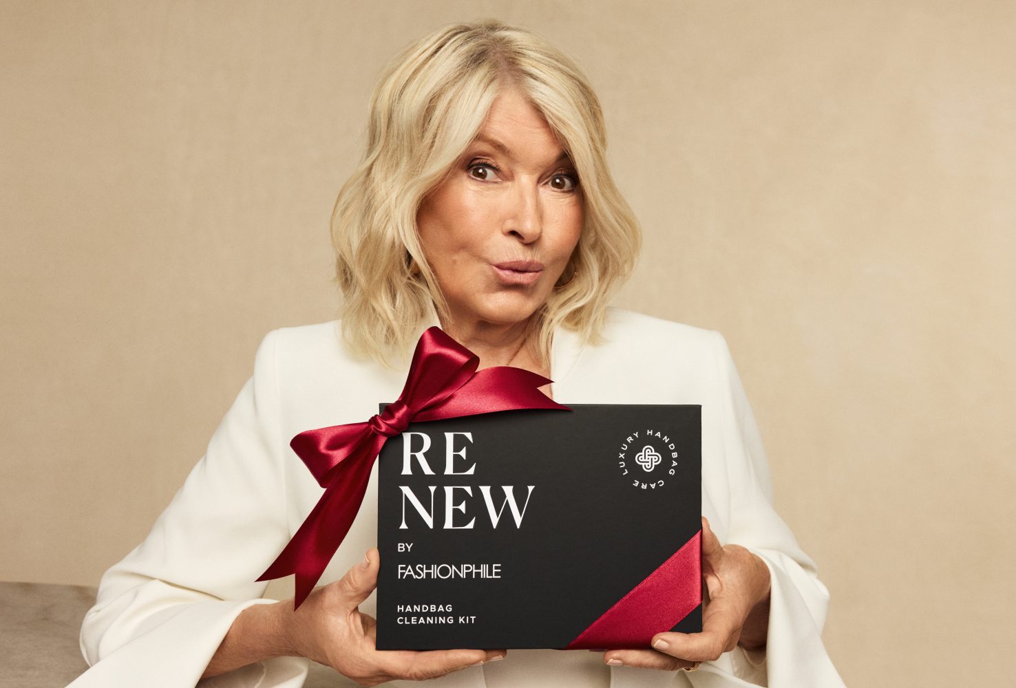 Martha Stewart in a white suit holding the ReNew Kit by FASHIONPHILE with a red bow on it