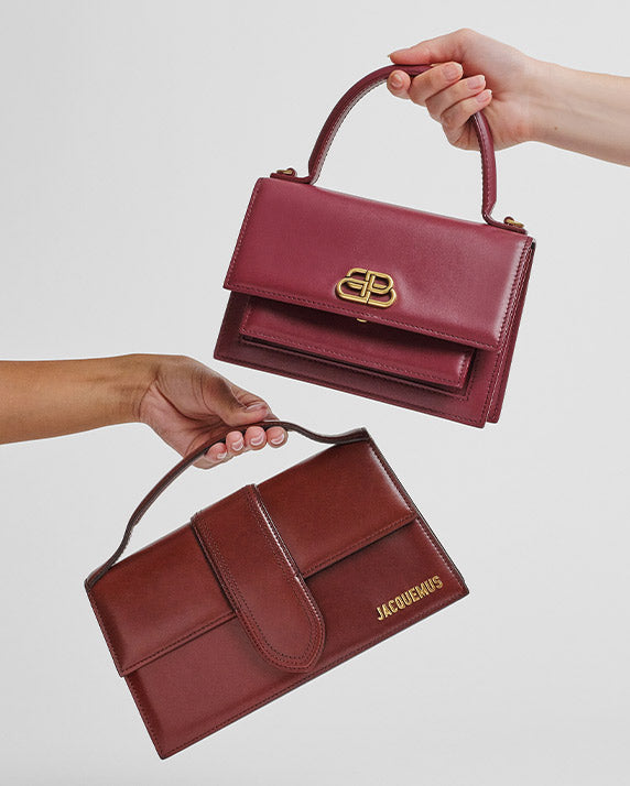 part of a woman's arm holding a brown Jacquemus Smooth Calfskin Le Grand Bambino bag and another part of a woman's arm holding a burgundy Balenciaga Box Calfskin XS Sharp Top Handle Bag