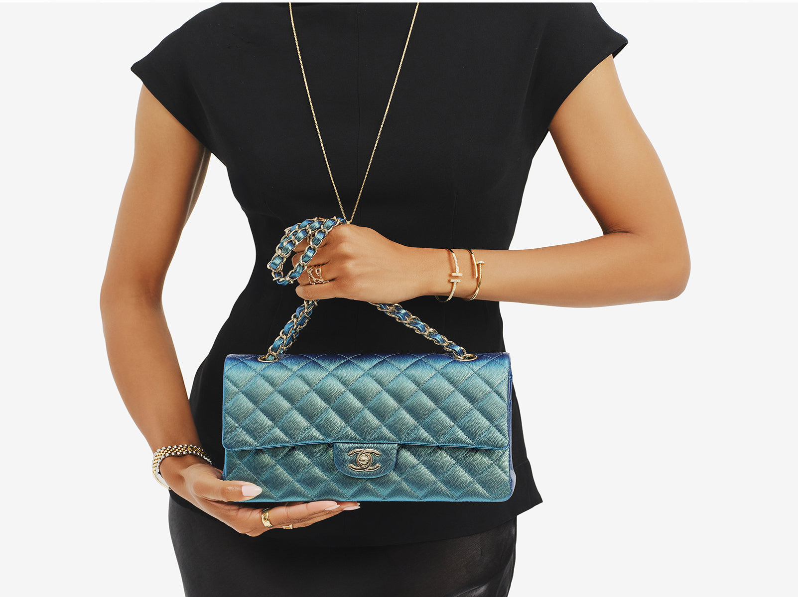 a woman wearing a black short sleeve dress and holding a Chanel green iridescent double flap bag