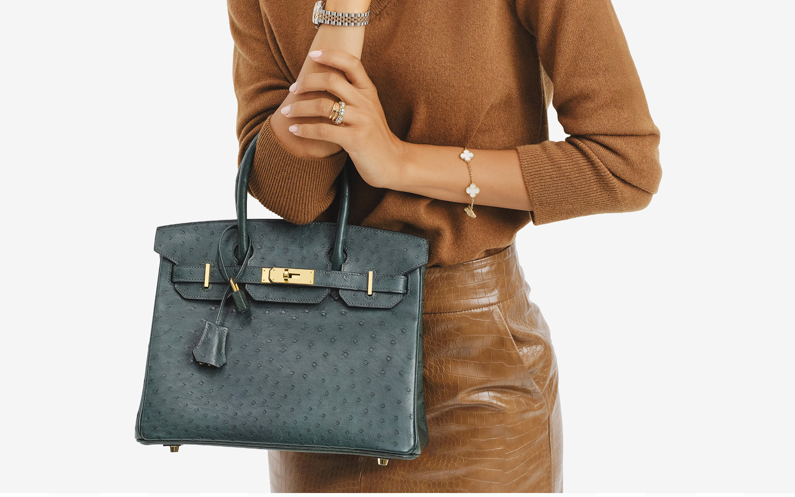 a woman wearing a tan sweater tucked into a tan leather skirt and she's holding a green ostrich Hermes Birkin 30 bag