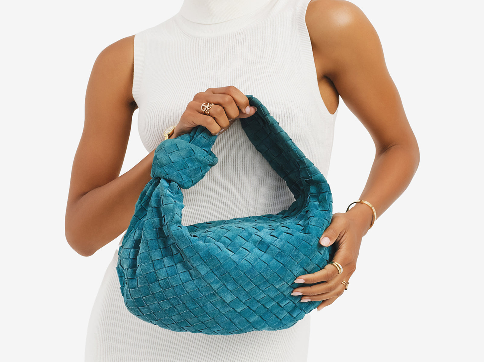 a woman wearing a white sleeveless knit turtleneck dress and holding a dark teal suede Bottega Veneta Jodie small hobo bag