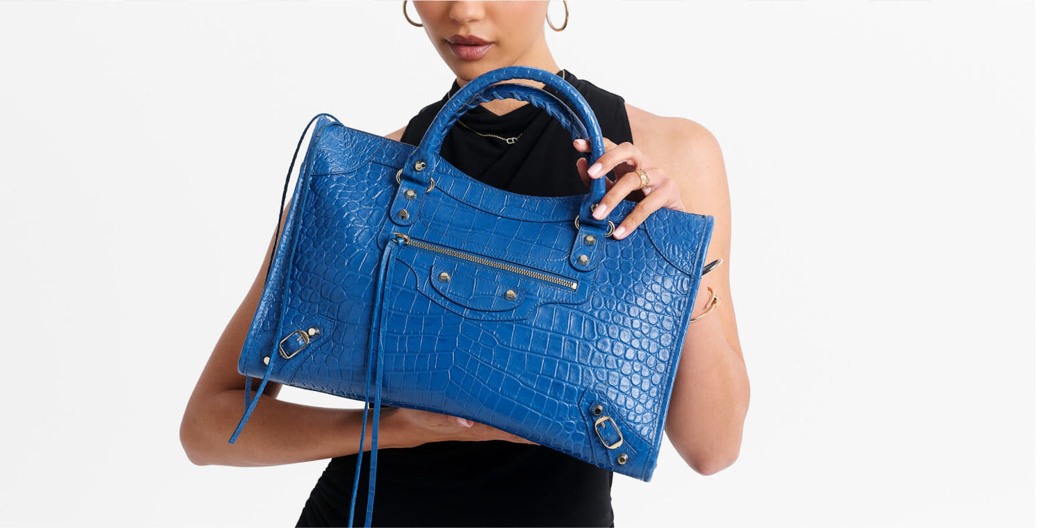 A model holds a bright blue crocodile-embossed leather handbag with silver-tone hardware against a plain white background.