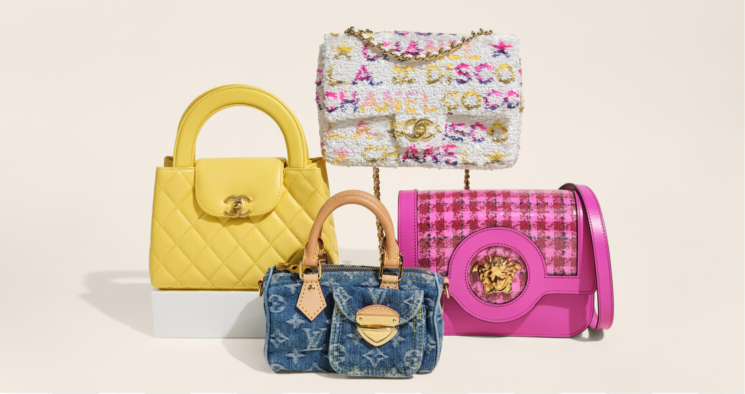 Four designer handbags arranged together on a light beige background: a yellow quilted top-handle bag on a white pedestal, a multicolor tweed shoulder bag hanging above, a blue monogram denim bag in front, and a bright pink houndstooth bag with gold hardware on the right.