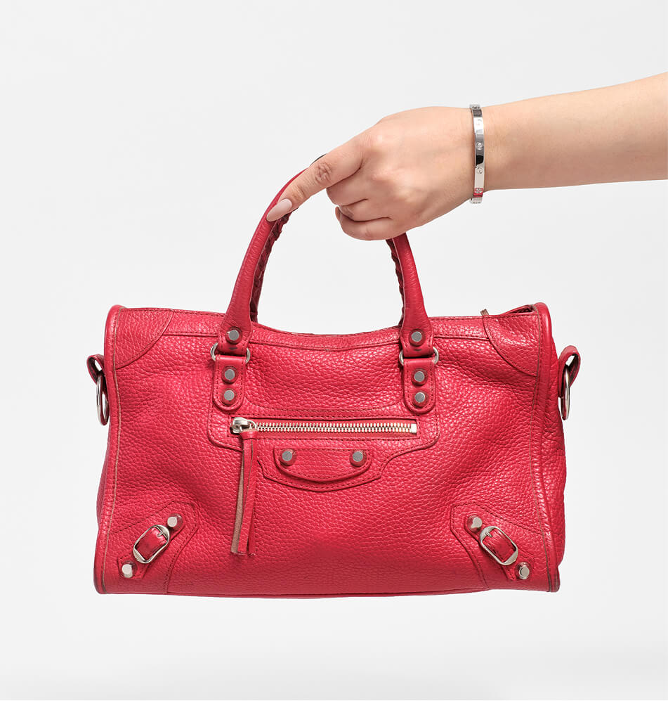 A bright red pebbled leather handbag with silver-tone hardware, held by a person's hand against a light gray studio background.
