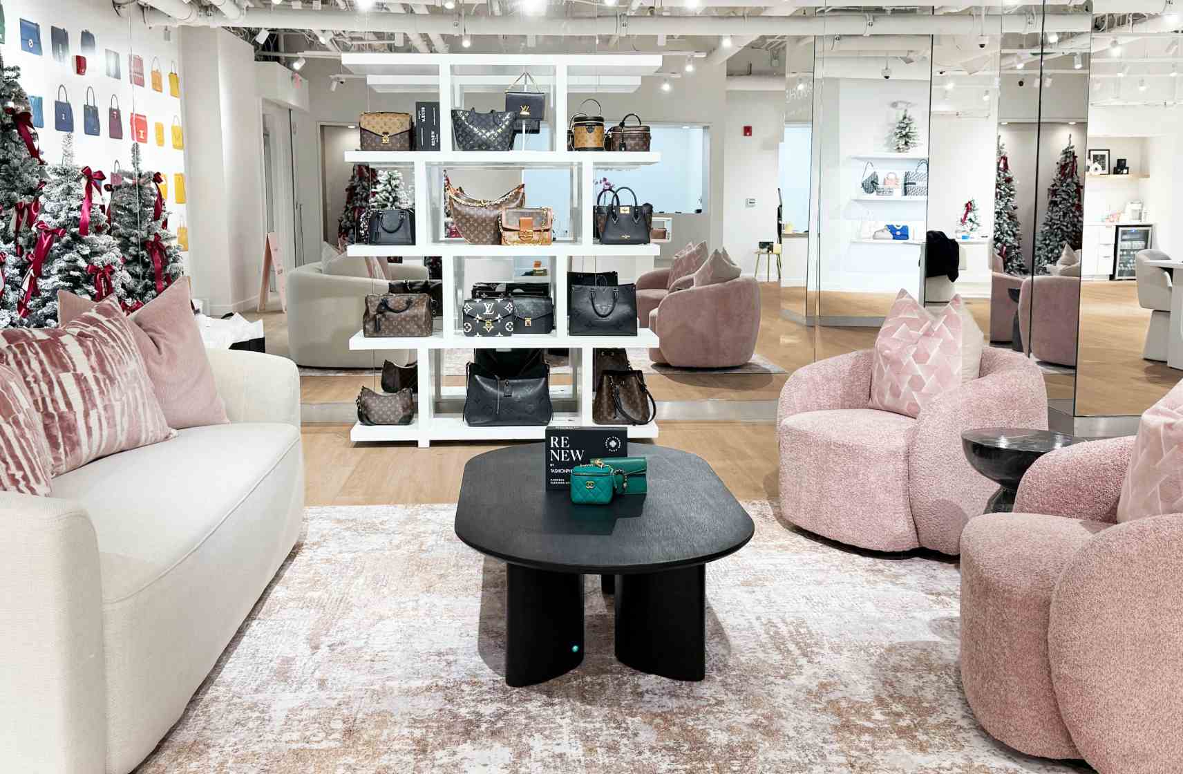 Luxury showroom with pink seating, a white display shelf of designer handbags, holiday décor, and mirrored walls
