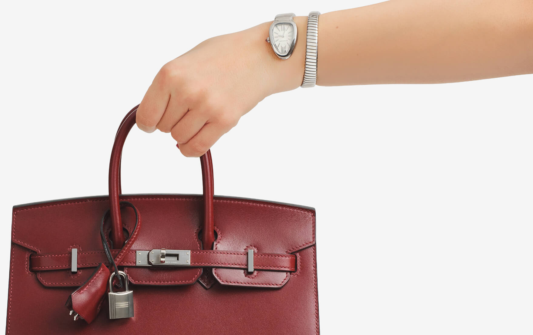 a woman's arm wearing a silver Bulgari Serpenti wrap watch and holding a burgundy color Hermes Sellier Birkin 25