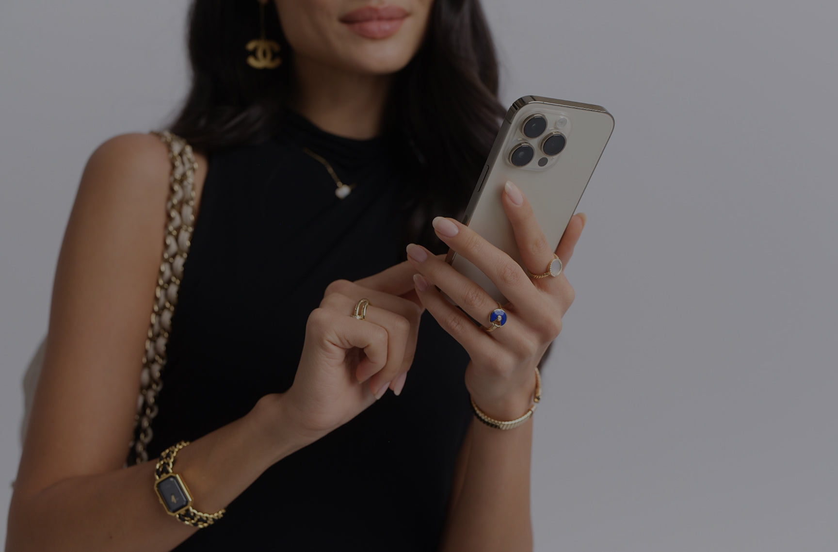 a woman wearing a black sleeveless dress and a yellow gold and black Chanel watch holding an iphone