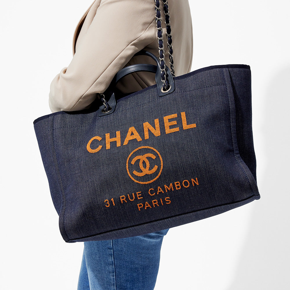 this is an image by FASHIONPHILE of a model wearing a dark navy blue large chanel deauville tote on her shoulder