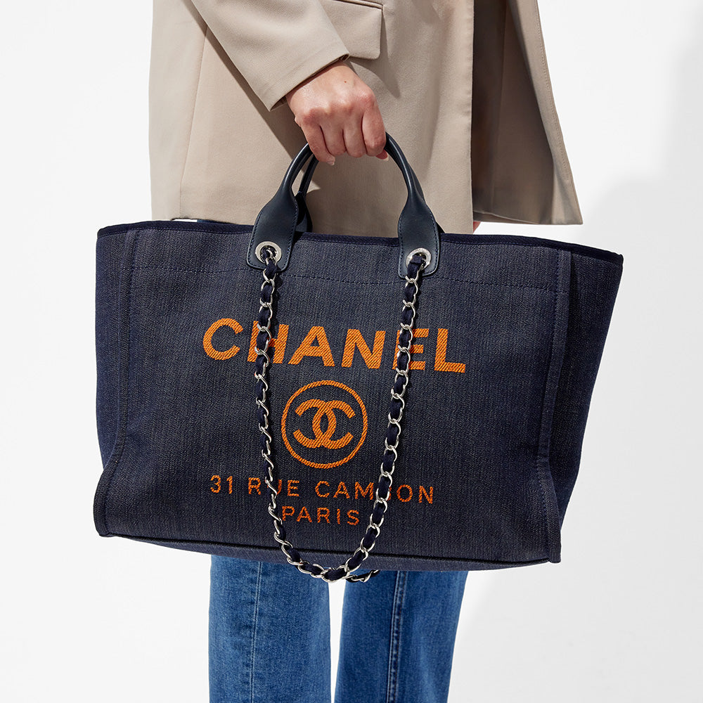 this is an image by FASHIONPHILE of a model holding a dark navy blue large chanel deauville tote in her hand