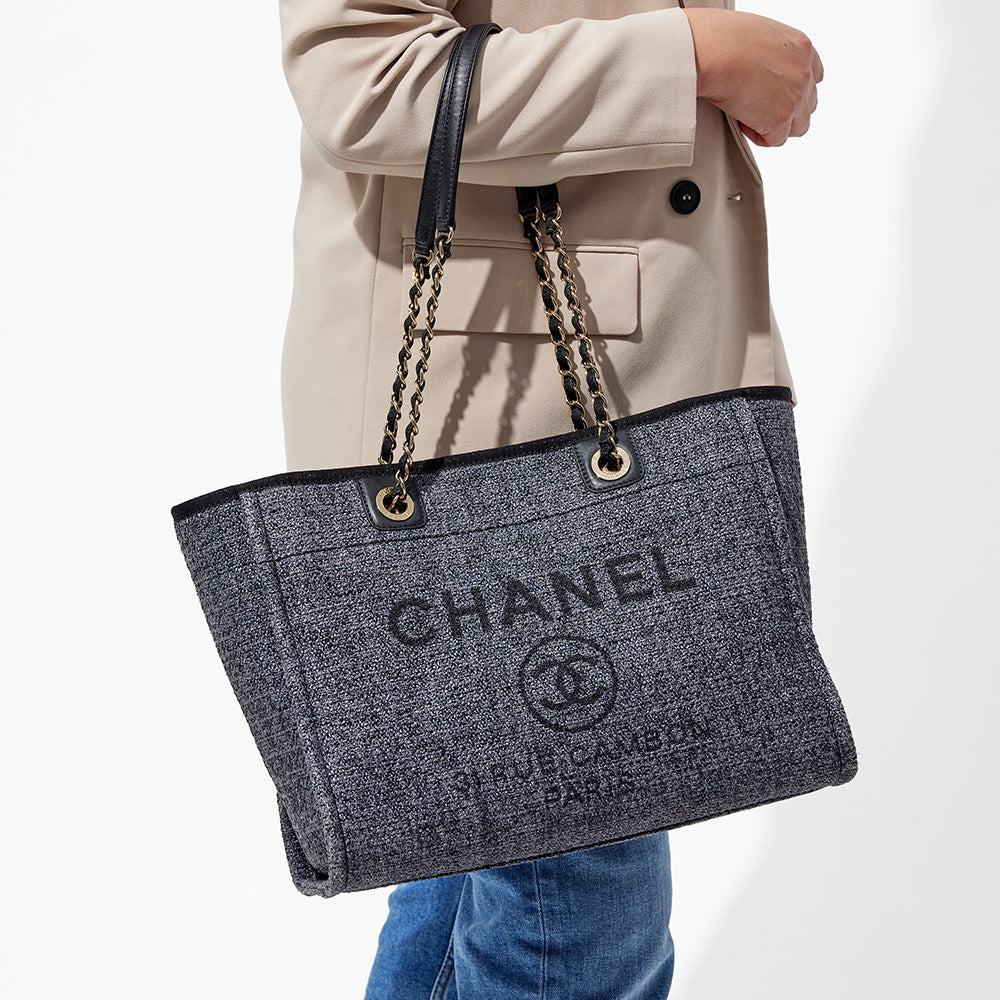 this is an image by FASHIONPHILE of a model wearing a dark navy blue small chanel deauville tote on her arm
