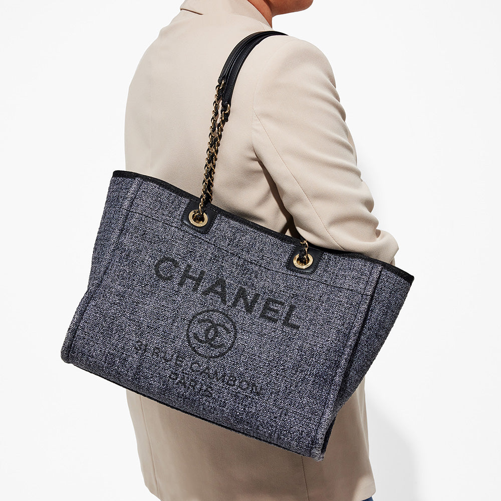 this is an image by FASHIONPHILE of a model wearing a dark navy blue small chanel deauville tote on her shoulder