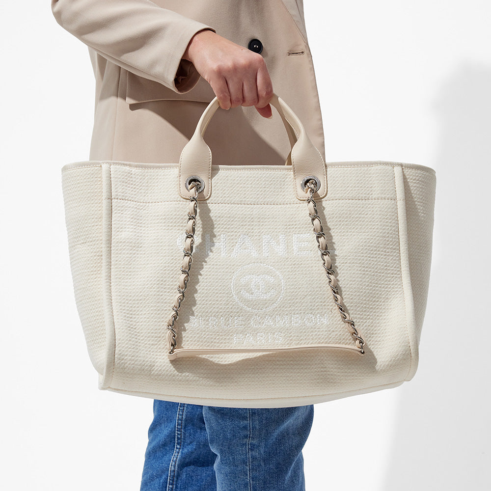 this is an image by FASHIONPHILE of a model holding a white medium chanel deauville tote in her hand